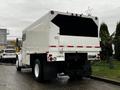 A 2007 Freightliner M2 106 truck with a white boxy cargo area and a flatbed design viewed from the rear facing right