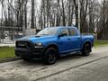 A blue 2021 RAM 1500 Classic pickup truck with a black front grille and black wheels parked on a street