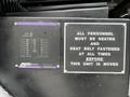 A control panel with a display showing various readings and a warning sign instructing personnel to be seated and fasten seat belts before moving the unit