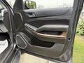 The interior door panel of a 2017 Chevrolet Tahoe featuring a black finish with wood accents and a control panel for windows and locks