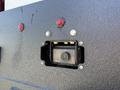 A close-up of a rear camera housing on a 2023 Ford F-550 with red lights and metallic screws around the black plastic cover