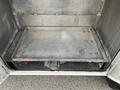A metallic cargo bed with a smooth surface and reinforced edges designed for a truck, featuring several mounting points and a small red valve on one side