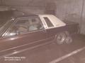 A 1982 Mercury Grand Marquis parked in a dimly lit area with a brown and cream exterior and one missing wheel