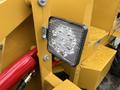 A close-up of a bright rectangular LED work light mounted on a yellow mini loader with visible hydraulic and metal components