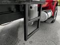 A metal bracket attached to the side of a red 2011 International 4400 truck near the exhaust pipe with a silver fuel tank visible behind it