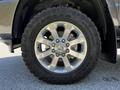 Close-up of a shiny silver alloy wheel with a prominent RAM logo on a 2022 RAM 3500 equipped with an all-terrain tire