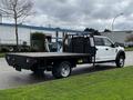 A 2017 Ford F-550 with a flatbed design and a black mesh safety barrier at the rear parked on a grassy area