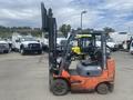 A 2010 Toyota 7FGGU25 forklift in orange color with a black operator seat and raised forks positioned for lifting