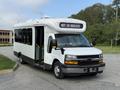 A 2020 Chevrolet Express bus with a white exterior and a front display reading NOT IN SERVICE parked with an open door and yellow interior steps visible