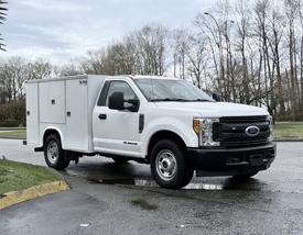 A white 2017 Ford F-350 SD with a utility body and an extended cab parked at an angle on a street