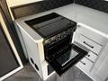 A black oven with a glass top and an open door revealing the interior is integrated into a white kitchen unit with modern hardware
