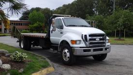 A white 2008 Ford F-750 flatbed truck with a chrome front grille and black wheels parked on a street