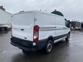 A white 2018 Ford Transit cargo van with a black lower section parked on a wet surface