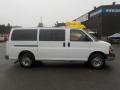 A white 2011 Chevrolet Express van with a long body and multiple windows on the sides parked with shiny chrome wheels and a clear view of its side profile