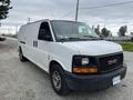 A white 2014 GMC Savana van with side cargo doors and a black front bumper parked on a gravel surface