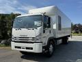A white 2024 Isuzu FVR truck with a boxy cargo area and chrome accents on the front grille and wheels