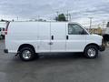 A white 2014 Chevrolet Express van with a sliding side door and visible marks on the body parked on a surface with reflection