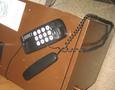 A corded telephone with a black body and a spiral cord features a keypad with numbers and symbols on the front and a separate handset resting nearby