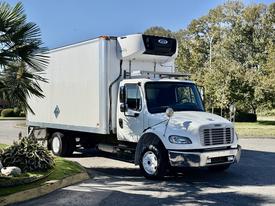 A white 2017 Freightliner M2 106 box truck with a refrigeration unit on top parked on a road