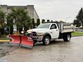 A 2012 Dodge Ram 5500 with a plow attached in front and a truck bed at the back parked on a wet surface
