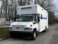 A white 2006 GMC C5000 truck with a large box-style body and a blue stripe on the side featuring a cab with a flat front and a light bar on top