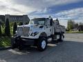 A 2011 International 7500 truck with a white cab and a flatbed equipped with a metallic container and safety lights on the roof