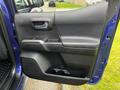 A blue 2022 Toyota Tacoma door interior featuring a black armrest a door handle and a speaker area with sleek design elements