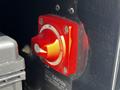 Close-up of a red battery disconnect switch on a 2022 Blue Bird BB Conventional bus with a black panel and caution label below the switch