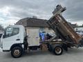 A 2008 Mitsubishi Fuso FE180 truck with a raised dump bed and a metallic body featuring a side door and large rear wheels