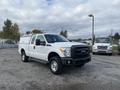 2015 Ford F-250 SD in white with a black grill and bed cover parked on gravel