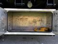 An open storage compartment of a 2012 Freightliner M2 112 with dirty metallic interior and a yellow strap resting inside