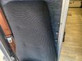 A black patterned seatback from a 2012 Ford Econoline van angled against a grey wall