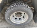 A close-up of a tire mounted on a silver wheel showing tread pattern and bolt configuration with part of the vehicle's body partially visible