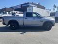 A silver 2021 RAM 1500 pickup truck is parked with the driver's side visible featuring black wheels and a distinctive RAM 1500 badge on the door