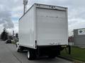 A white 2006 Hino 268 truck with a boxy cargo container and a flatbed rear is parked on the street