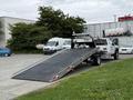 A 2022 Ford F600 tow truck with a lowered flatbed is positioned at an angle, ready to load a vehicle onto its ramp