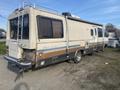 A 1987 Chevrolet Fleetwood Pace Arrow motorhome with a beige exterior featuring blue and brown stripes and large windows on the side