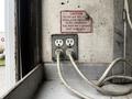 A close-up of two electrical outlets with exposed wires and a caution sign above them advising against use in wet conditions