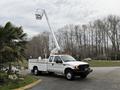 A white 2001 Ford F-350 bucket truck with an extended lift arm and utility bed is parked with a raised boom and safety lights on top