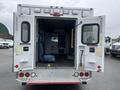 A 2016 Chevrolet Express ambulance with double rear doors open revealing the interior space containing seats and medical equipment