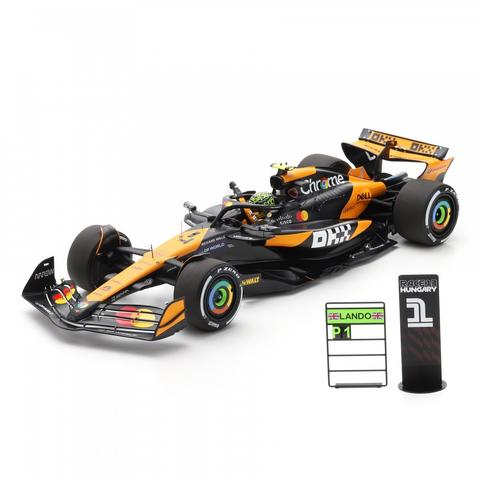 A model car of the Spark McLaren MCL38 featuring the #4 L. Norris design with orange and black details and sponsor logos on the bodywork