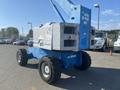 A blue 1997 Genie S-65 4X4 aerial lift with large black tires and a raised boom arm in the rear, featuring hydraulic controls and machinery components visible on the side