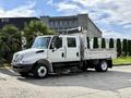 A 2012 International 4300 truck with a flatbed and dual rear wheels is parked with a cab that has seating for multiple passengers