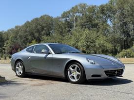 A silver 2005 Ferrari 612 Scaglietti with a sleek design and polished alloy wheels is parked at an angle showcasing its sporty profile
