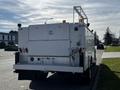 A 2018 Ford F-550 utility truck with a white body featuring multiple lights and a ladder rack on top viewed from the rear