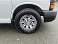 A silver 2012 Chevrolet Express van with a shiny chrome wheel and a black tire featuring the Chevrolet logo on the side