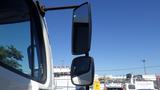 Close-up of a 2015 Freightliner M2 106 side mirror with a clear blue sky above and a visible truck cabin structure on the left