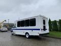 A white 2015 Chevrolet Express shuttle bus with a blue stripe along the side and multiple rear windows