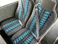Two fabric-covered bus seats with blue and gray patterns and seatbelts positioned on the side of a bus interior