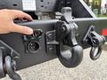 A hand reaching toward the heavy-duty hook mounted on a black truck chassis with various attachments including an electrical socket and a metal latch